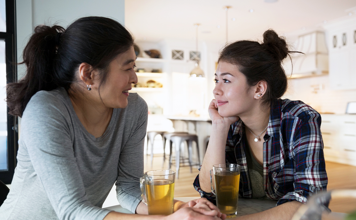 Mother and teenage daughter holding hands drinking tea.
