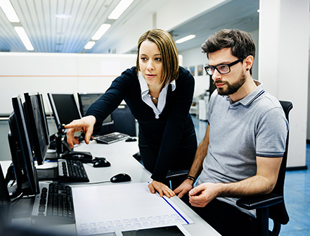 Two IT professionals in a big control room of a factory talking.