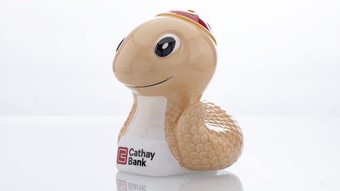 Creada para la promoción de 2025, la alcancía con forma de serpiente representa una serpiente de color naranja claro con una gorra roja y el logotipo de Cathay Bank en el pecho.